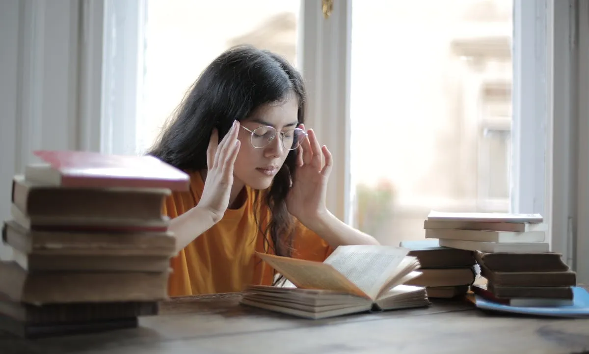 Femme épuisée entourée de piles de livres, illustrant la surcharge cognitive et la fatigue mentale TDAH