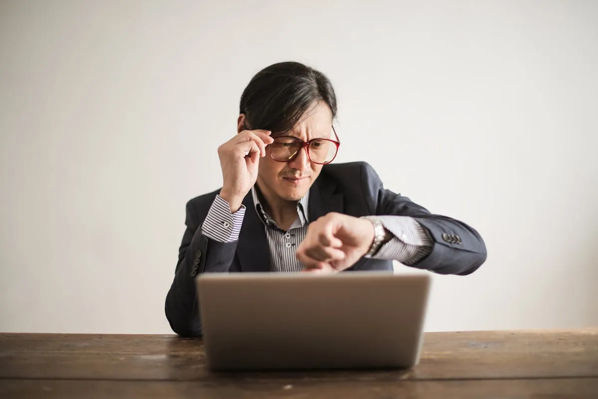 Homme ajustant ses lunettes en regardant sa montre devant son ordinateur, illustrant la time blindness TDAH